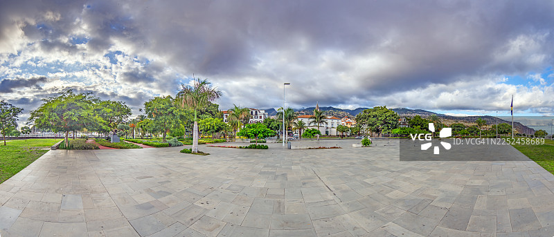 葡萄牙马德拉群岛，广阔的空广场，四周环绕着郁郁葱葱的绿树和建筑，天空布满戏剧性的云彩图片素材