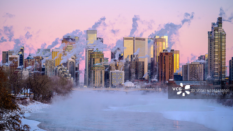 加拿大卡尔加里，寒冷冬季日落时分，摩天大楼林立的城市天际线和河流的全景，建筑和水面升腾着蒸汽图片素材