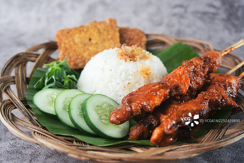 美味的印尼烤鸡饭配沙爹和新鲜黄瓜片，盛放在传统的编织盘上图片素材