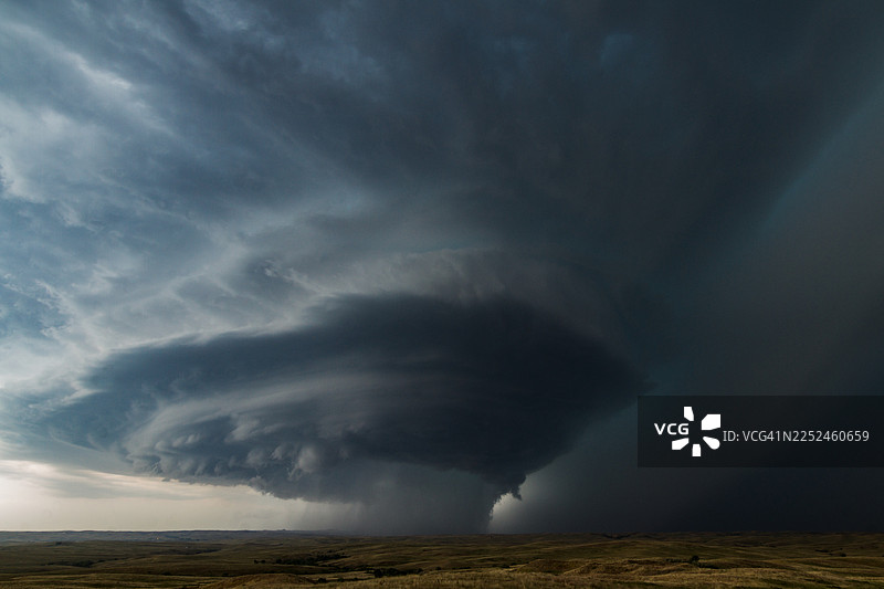 广阔的开放景观上聚集着戏剧性的风暴云，黑暗的漩涡状云层预示着恶劣天气图片素材