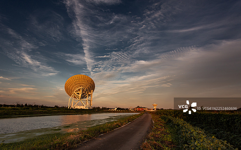 上海，中国，夕阳映衬下的戏剧性天空，乡村背景下的巨大射电望远镜，伴有道路和运河的风景。图片素材