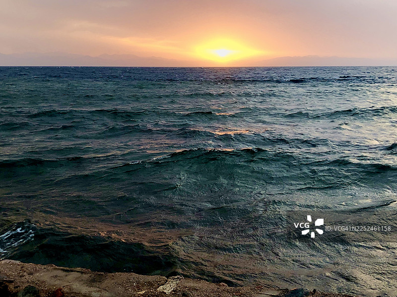 夕阳下宁静的海景，映衬着生机勃勃的天空，温柔的海浪反射着温暖的光芒图片素材