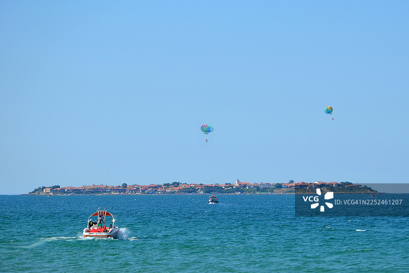 晴朗的夏日，人们在保加利亚历史悠久的岛屿小镇附近享受帆伞运动和划船的乐趣图片素材