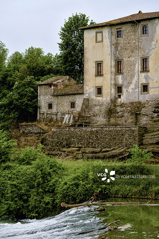 古老的石制建筑坐落在俯瞰河流的岩石峭壁上，周围绿叶葱郁图片素材