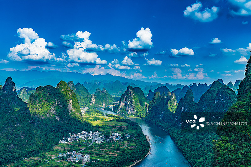 中国桂林，漓江蜿蜒穿过壮丽的喀斯特山峰和一座小村庄的广角全景，天空湛蓝，点缀着云彩。图片素材