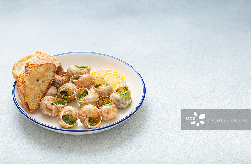 俯视视角拍摄的美味蒜蓉黄油蜗牛配欧芹，搭配新鲜面包和柠檬片，盛放在白盘上图片素材