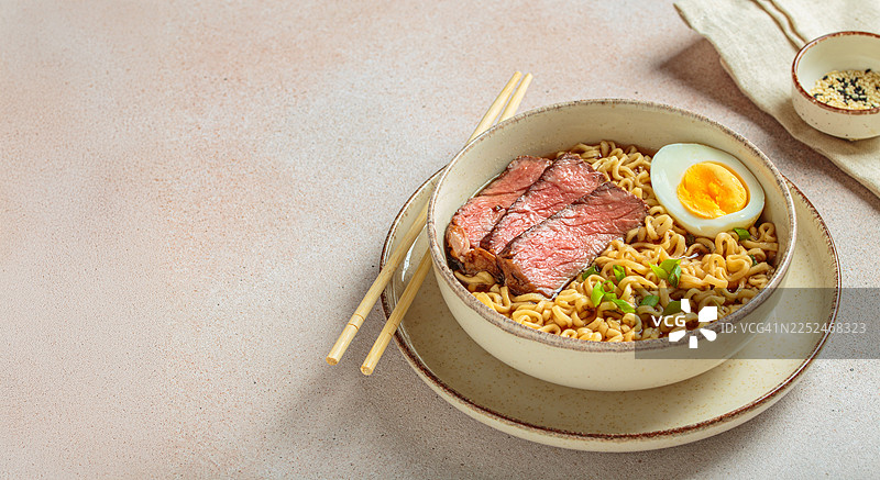 美味的拉面汤，配有切片牛肉和煮鸡蛋，用葱花点缀，并配有筷子图片素材