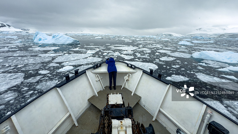 高角度俯瞰，一个人在一艘船上，在多云天空下，于南极洲寒冷的海域中，穿越冰山和浮冰。图片素材