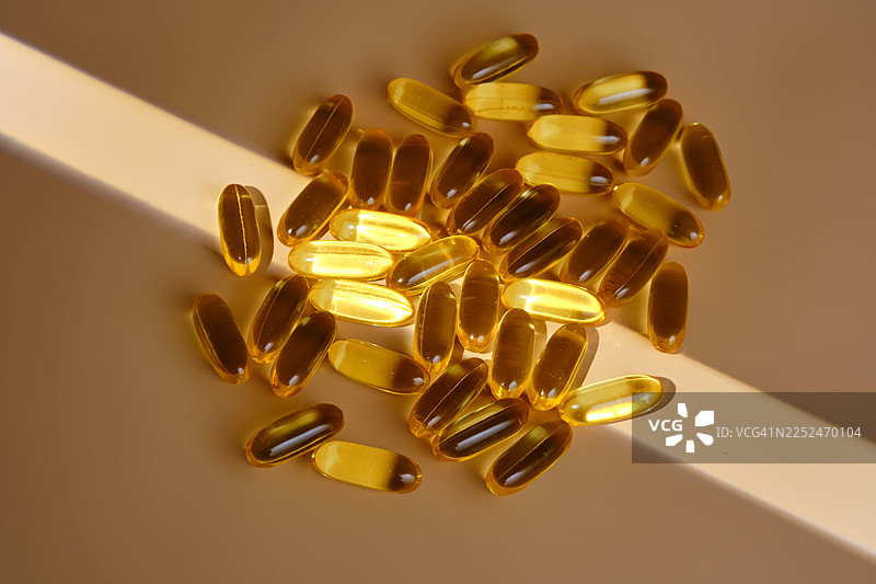 高角度拍摄的许多黄色胶囊散落在米色表面上，一道光束扫过它们图片素材