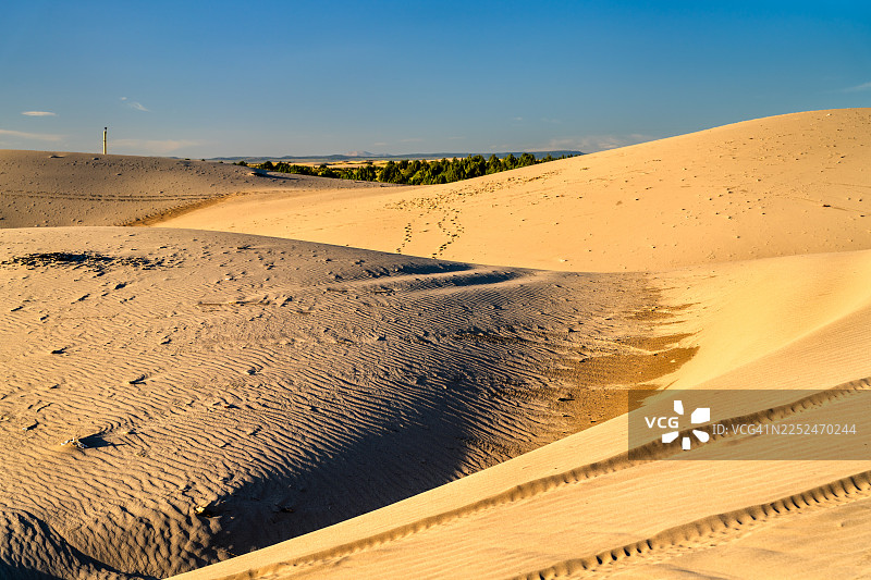 晴朗蓝天下广阔沙漠沙丘的风景，沙地上有淡淡的脚印和车辙图片素材