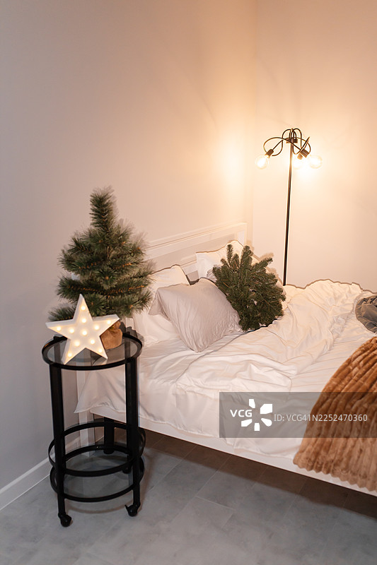 舒适的卧室，圣诞节装饰着节日彩灯，床头柜上放着一棵小圣诞树图片素材