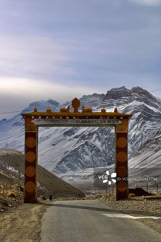 前景是传统拱门和蜿蜒的道路，背景是白雪皑皑的山脉风景，印度卡扎图片素材