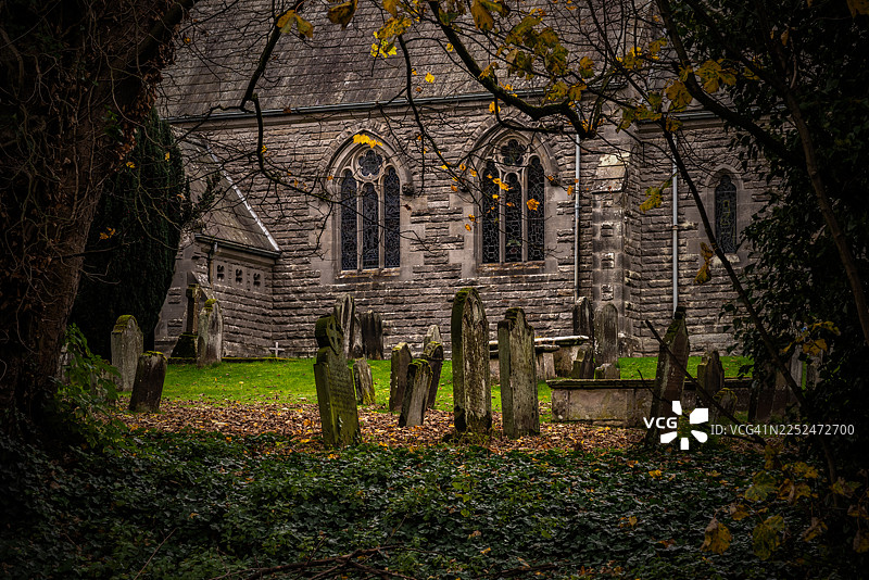 秋季古老的教堂建筑和墓地，有墓碑和落叶，英国基尔代尔图片素材