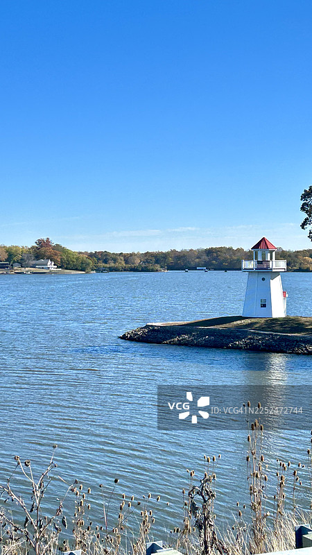 美国斯普林菲尔德，岩石海岸上带有红色屋顶的白色灯塔，四周是平静的蓝色大海，天空晴朗图片素材