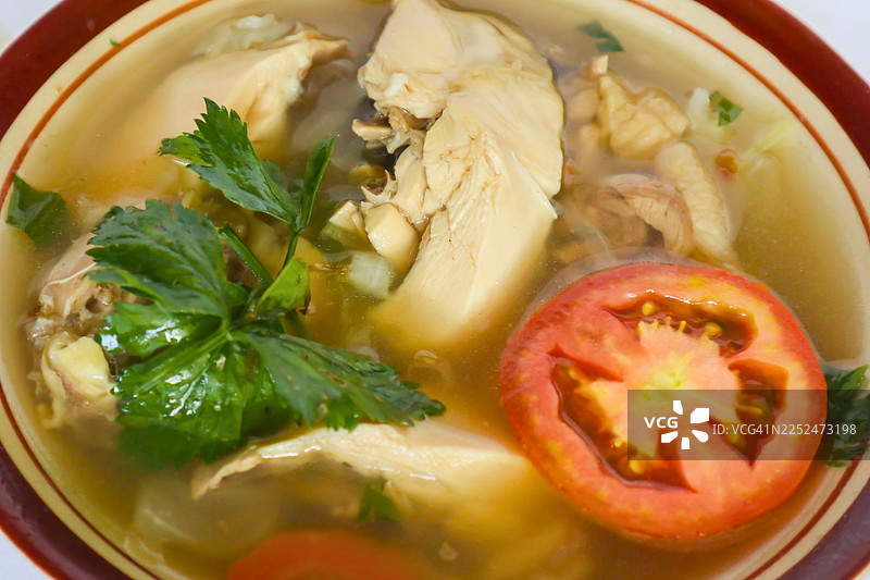 桌上一碗美味鸡汤的俯视视角，配有新鲜香草和番茄片，正待上桌图片素材