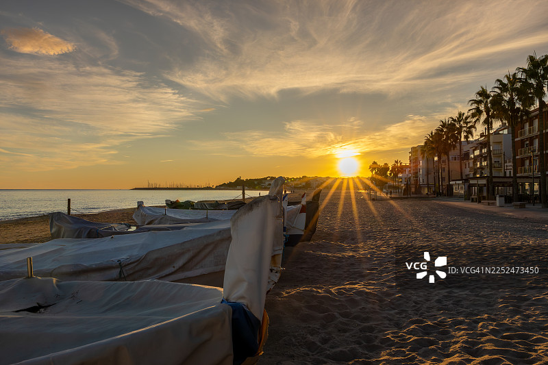 金色的日落映照在沙滩上，海边的船只和棕榈树旁是建筑物，地点：西班牙托雷德姆巴拉图片素材