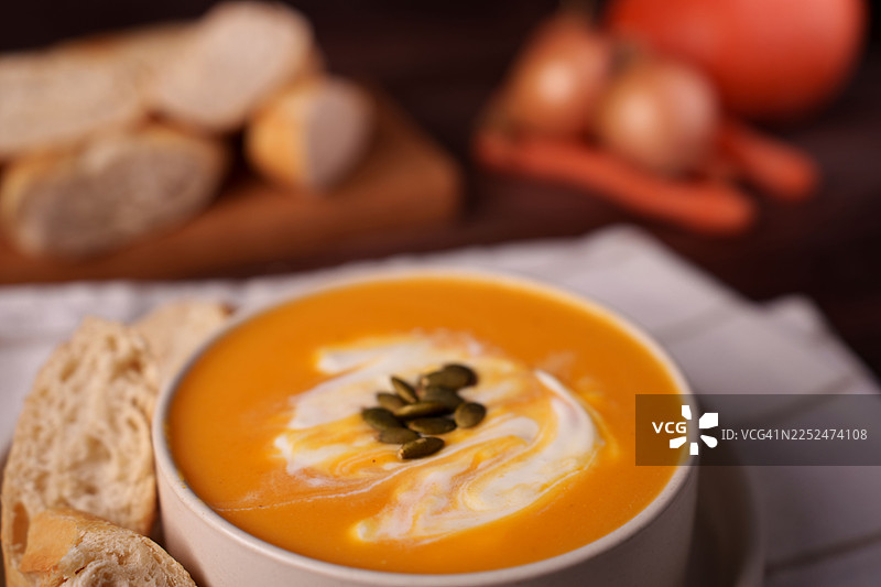 乡村餐桌上美味的手工南瓜汤，配有奶油、南瓜籽和硬皮面包图片素材