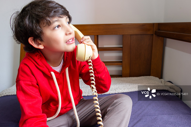 年轻男孩在家中使用老式固定电话打电话。图片素材