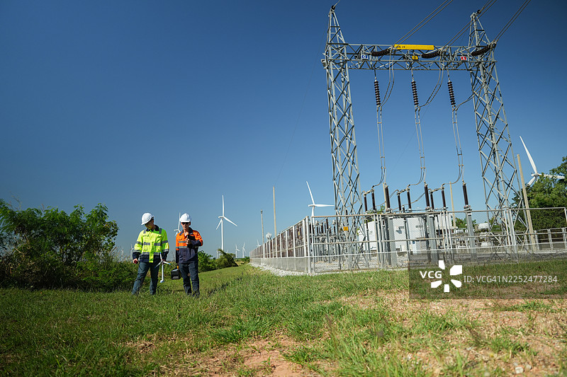 工程师正在检查一座大型风力发电机的运行情况，该发电机正在风力发电场中发电。图片素材