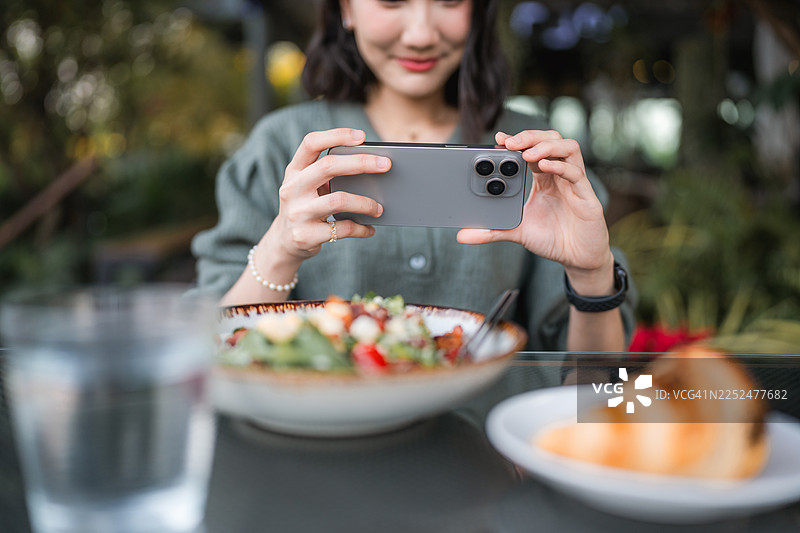 一位开朗的年轻女子在咖啡馆用手机给她的食物拍照图片素材