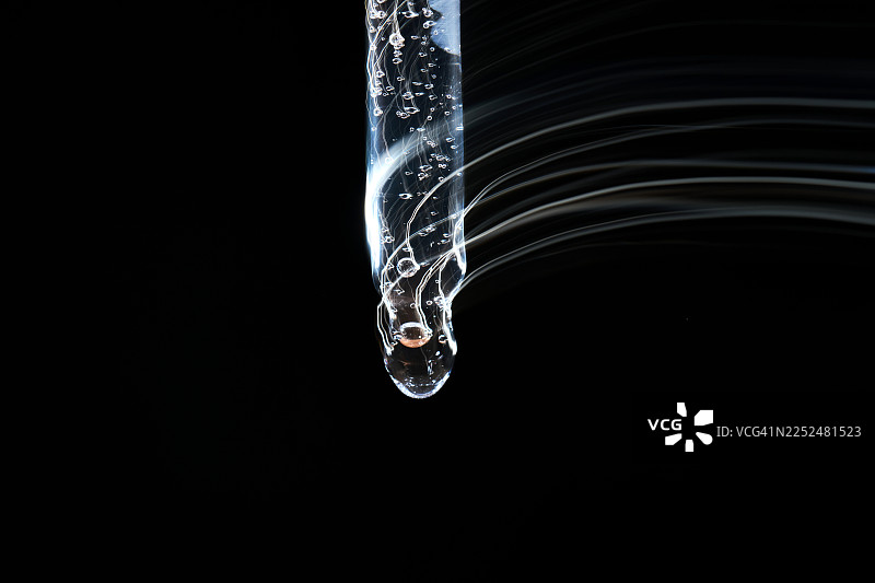 透明液体精华从滴管中滴落，带有光轨图片素材