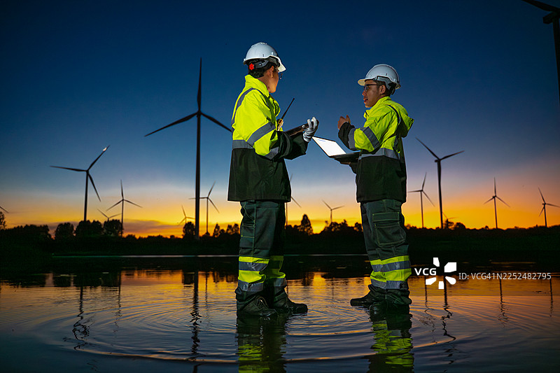 剪影工程师在风电场工作，监控可再生能源运营，风力涡轮机象征着可持续技术和清洁能源解决方案，以及可再生能源行业内的环境责任。图片素材