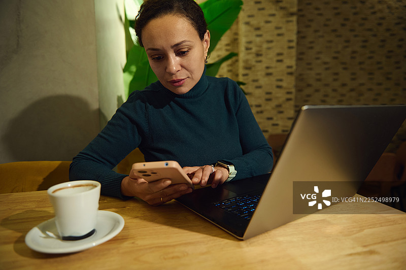 中东女性在舒适的咖啡馆用笔记本电脑和手机远程办公图片素材