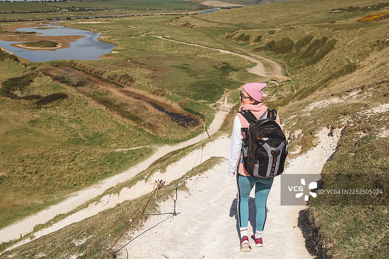 一名女徒步者沿着悬崖小径行走，俯瞰着山谷图片素材