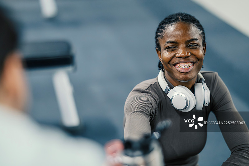 佩戴牙套的年轻女子在健身房戴着耳机微笑图片素材