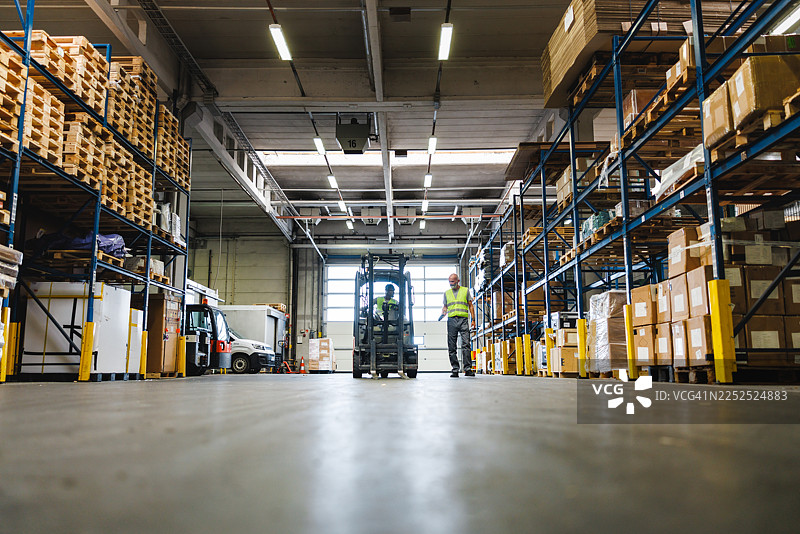 繁忙的仓库场景，工人们在堆叠的货架和托盘之间操作叉车图片素材