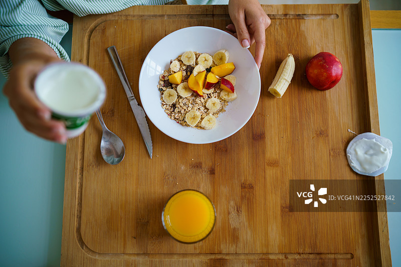 俯视视角，女性手正在准备健康的早餐，包含谷物、水果和酸奶。图片素材