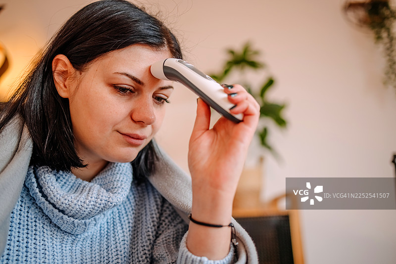 一名女子在家中的客厅里，在感冒时测量体温，关注自己的健康图片素材