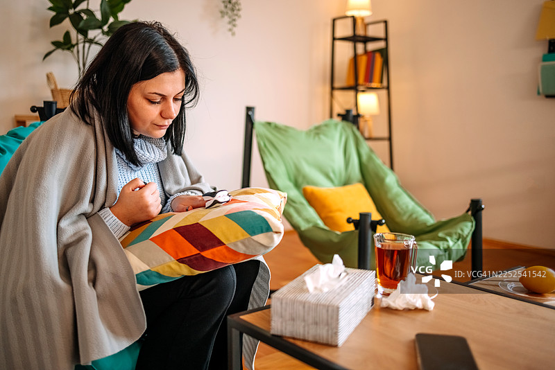 一名女子在家中的客厅里检查自己的健康状况，她患有感冒。图片素材