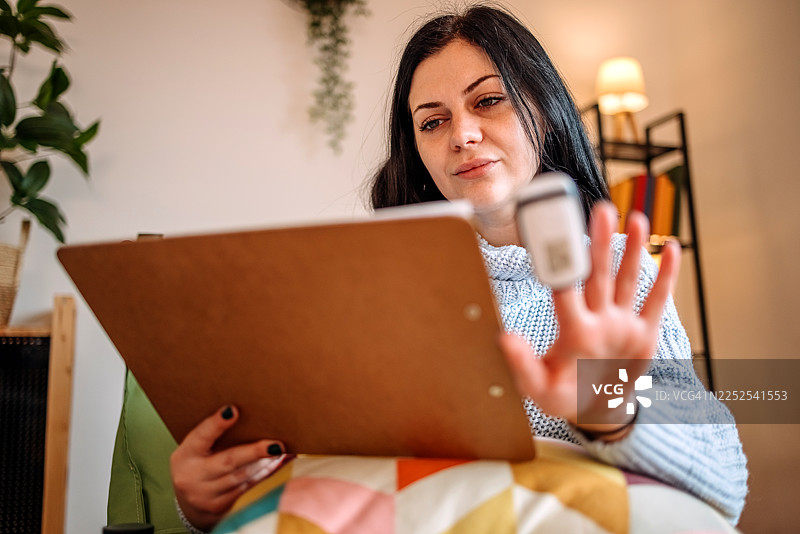 一名女子在家中的客厅里查看自己的健康状况，她患有感冒。图片素材