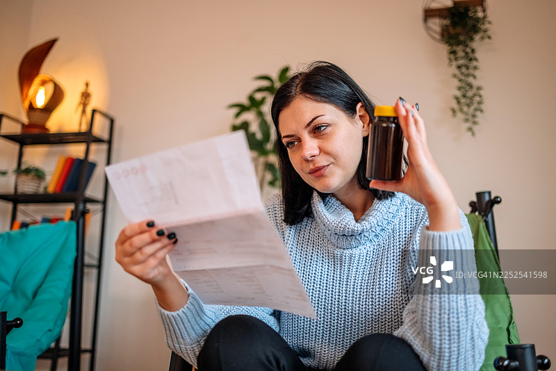一名女子在家中的客厅查看她的健康状况，并看着药瓶。图片素材