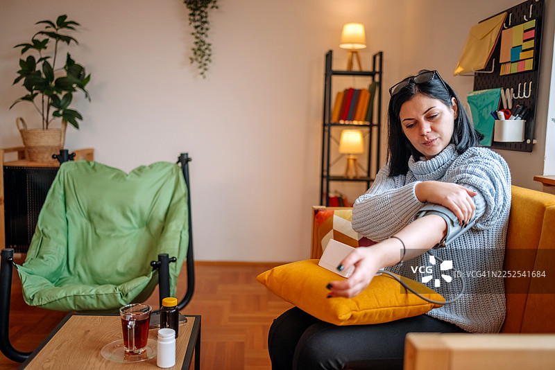 一位女士在家中客厅使用血压计测量健康状况图片素材