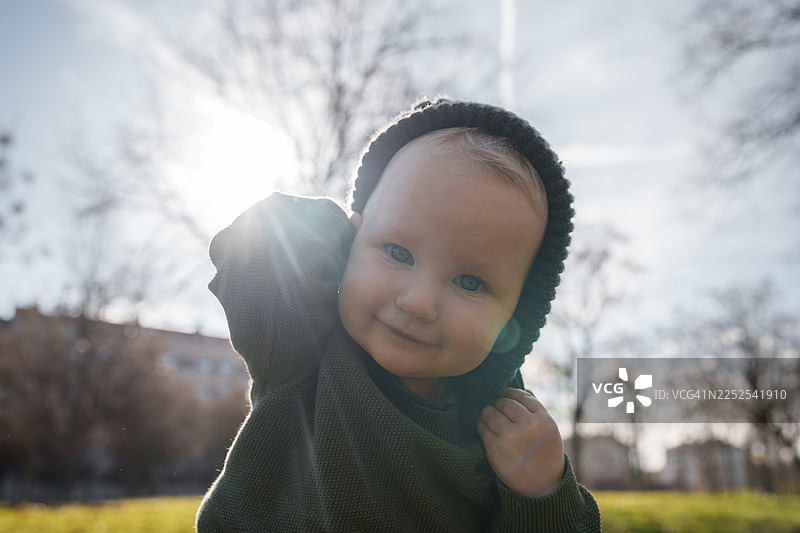 秋日暖阳下，一个穿着针织帽的快乐小宝贝在宁静的公园里微笑。图片素材