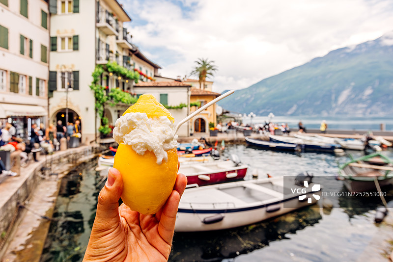 一个人拿着柠檬冰淇淋，冰淇淋盛放在新鲜的柠檬中，个人视角，意大利加尔达湖畔的加尔达镇图片素材
