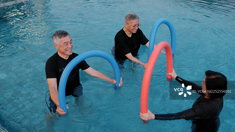 一群老年人在游泳池中使用浮条进行物理治疗锻炼图片素材