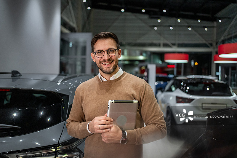 汽车销售人员在汽车展厅里微笑着拿着平板电脑图片素材