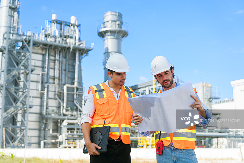 工程师在工业炼油厂讨论蓝图和笔记本电脑。图片素材
