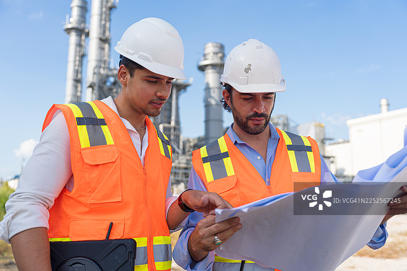 工程师在炼油厂讨论蓝图和笔记本电脑。图片素材