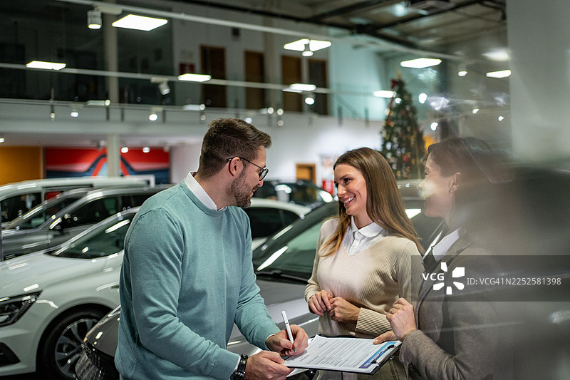 一对情侣在汽车经销商处购买汽车并签署销售合同图片素材
