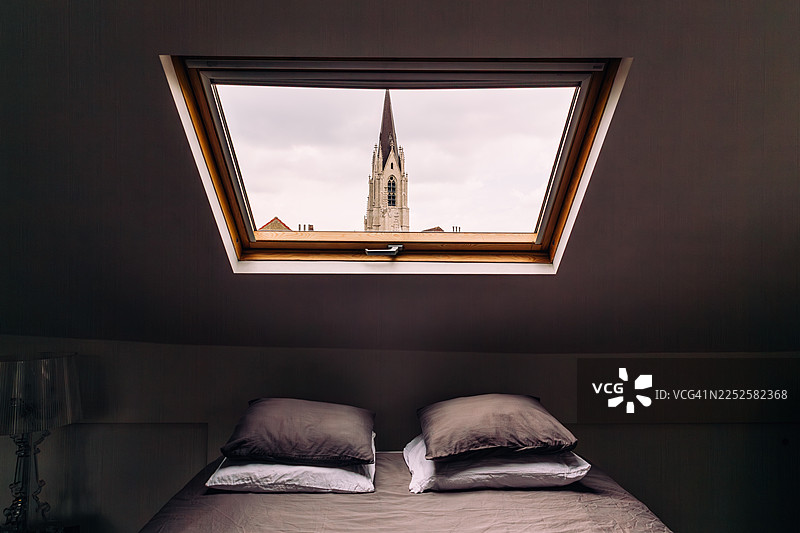 床上的枕头和阁楼的窗户，窗外是老城天际线图片素材