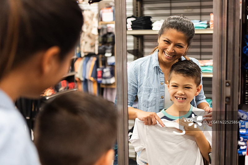 快乐的母子俩在服装店里购物，面带微笑。图片素材