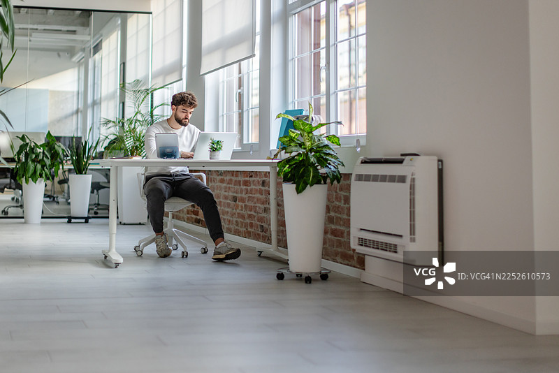 白天，年轻人在现代办公室环境里，伴着植物和自然光，独自工作图片素材
