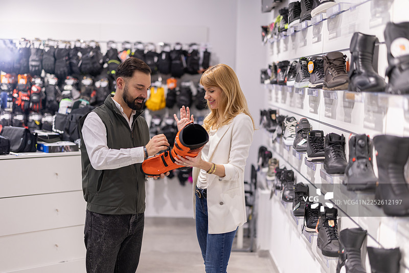 一对情侣在鞋店里试穿亮橙色靴子，他们的朋友们今天也一起在此选购靴子。图片素材