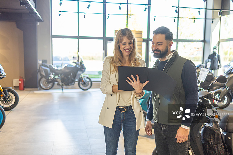 快乐情侣在展厅里一边友好地讨论生意，一边翻阅摩托车目录图片素材