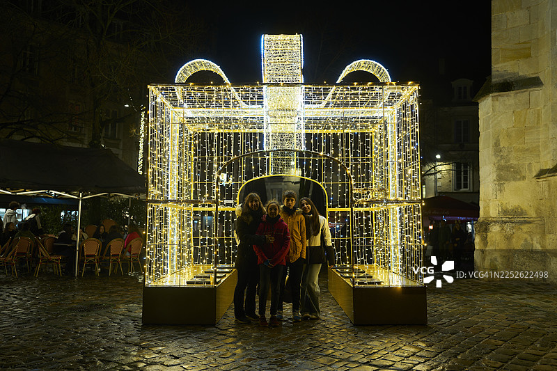 夜晚，朋友们站在巨大的礼品盒和串灯旁图片素材