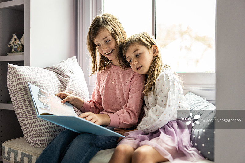 姐姐在窗边的角落给妹妹读书图片素材